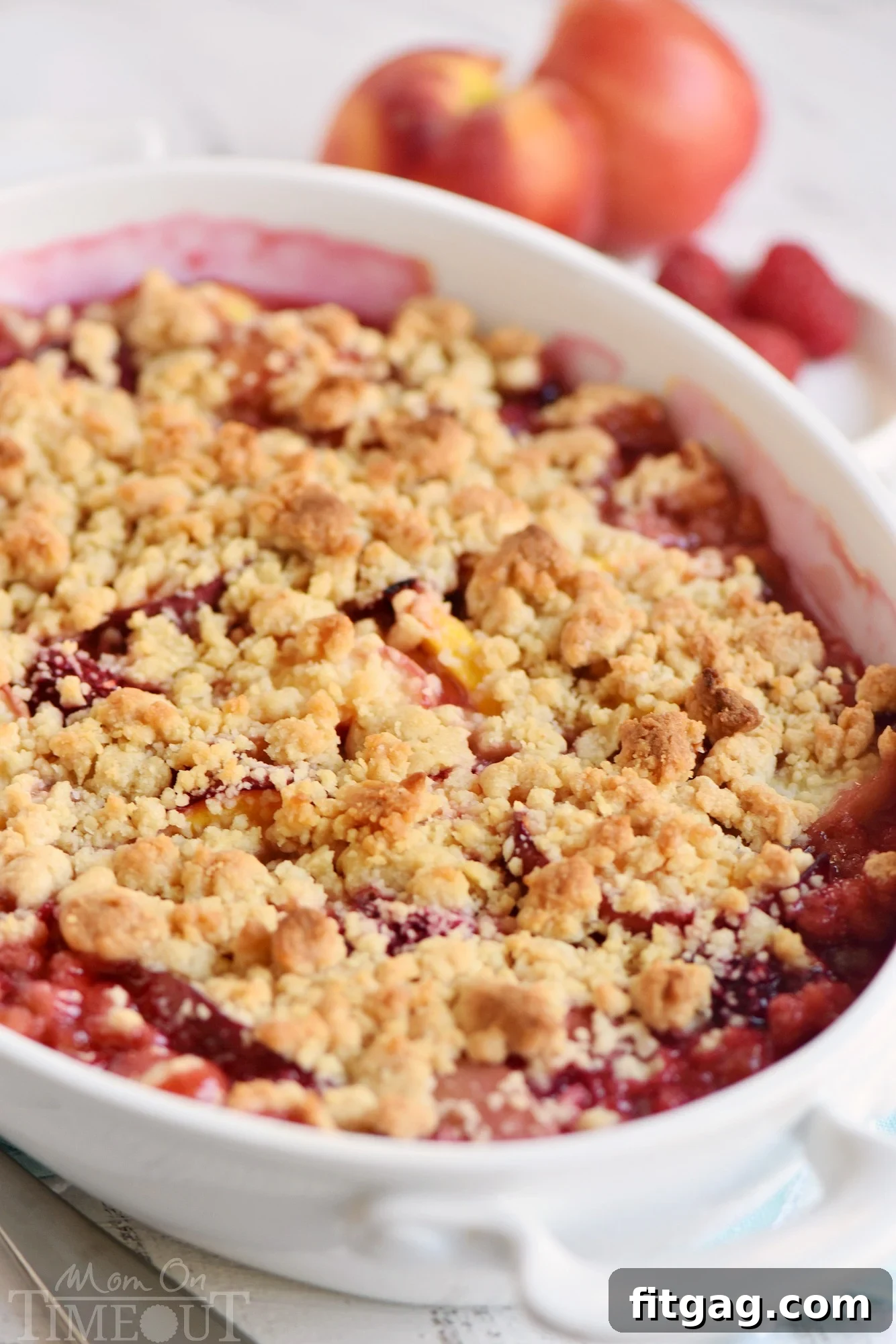 Close-up of a raspberry peach crumble with a golden-brown crumb topping in a ceramic casserole dish before baking.