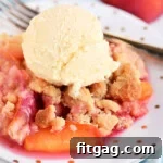 A serving of raspberry peach cobbler on a white plate, topped with a large scoop of vanilla ice cream.