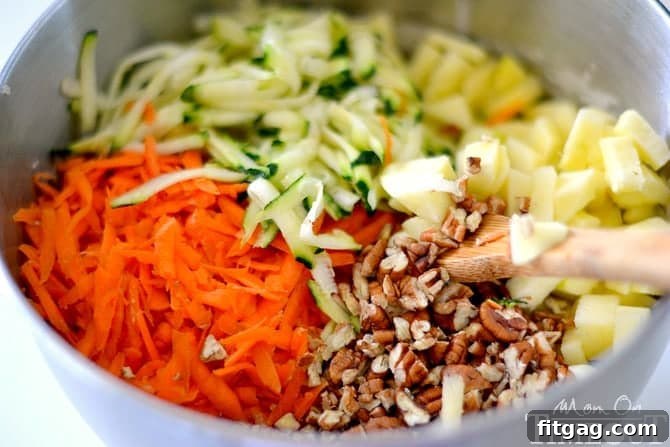Bowl of shredded carrots, zucchini, diced apples, and chopped pecans ready for mixing into the bread batter.