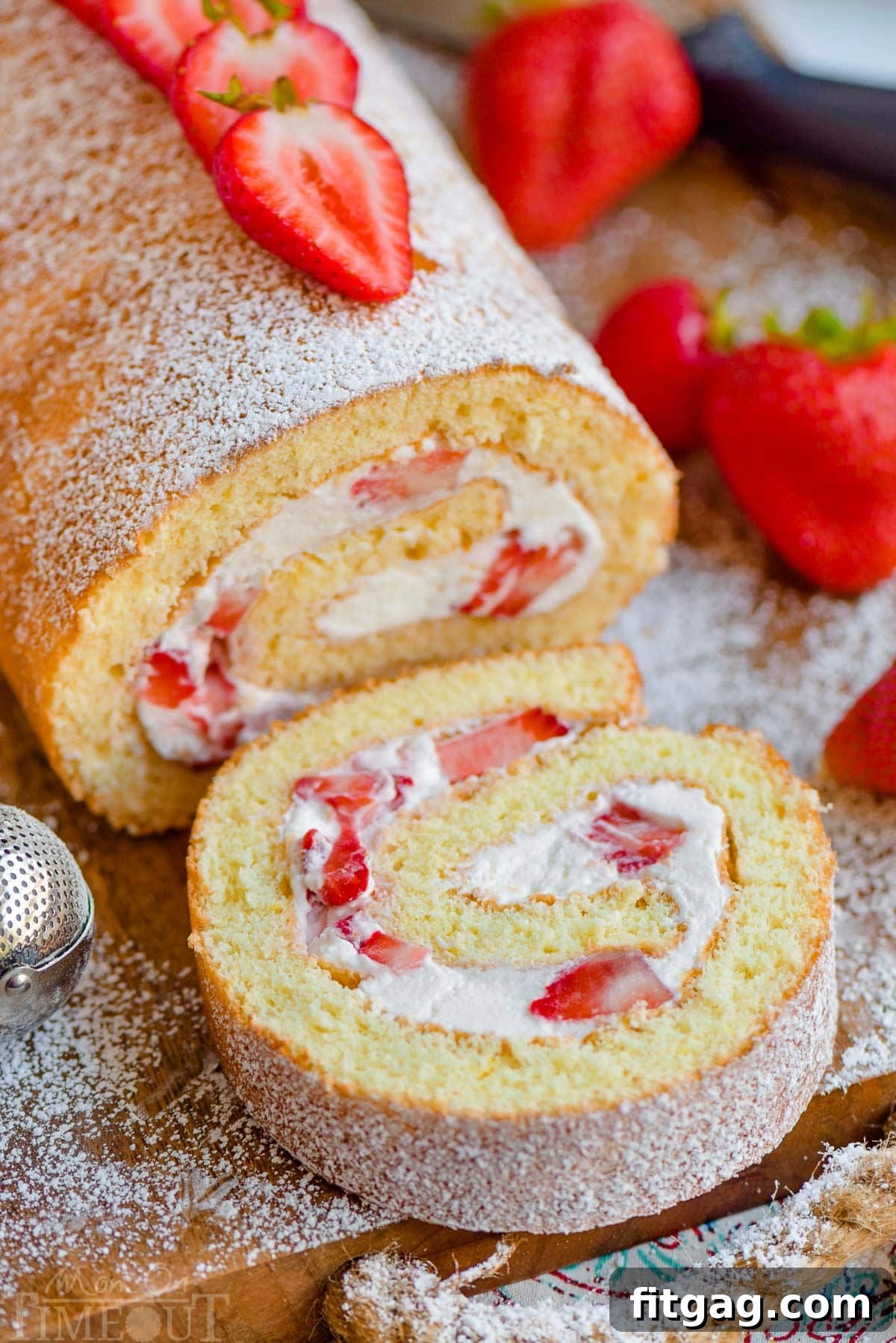 Close up view of strawberry shortcake roulade with one slice of cake cut off. Fresh strawberries on top of cake.