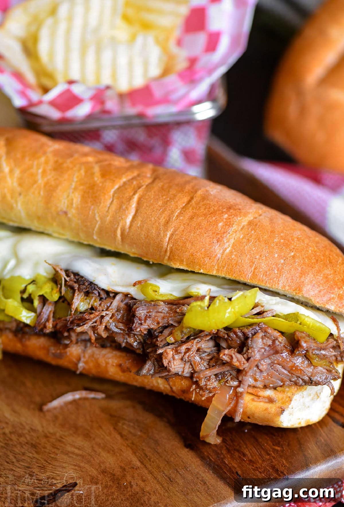 Melt-in-Your-Mouth Slow Cooker Italian Beef Sandwiches 2 Italian Beef Sandwich sitting on wood cutting board with a basket of chips behind it.