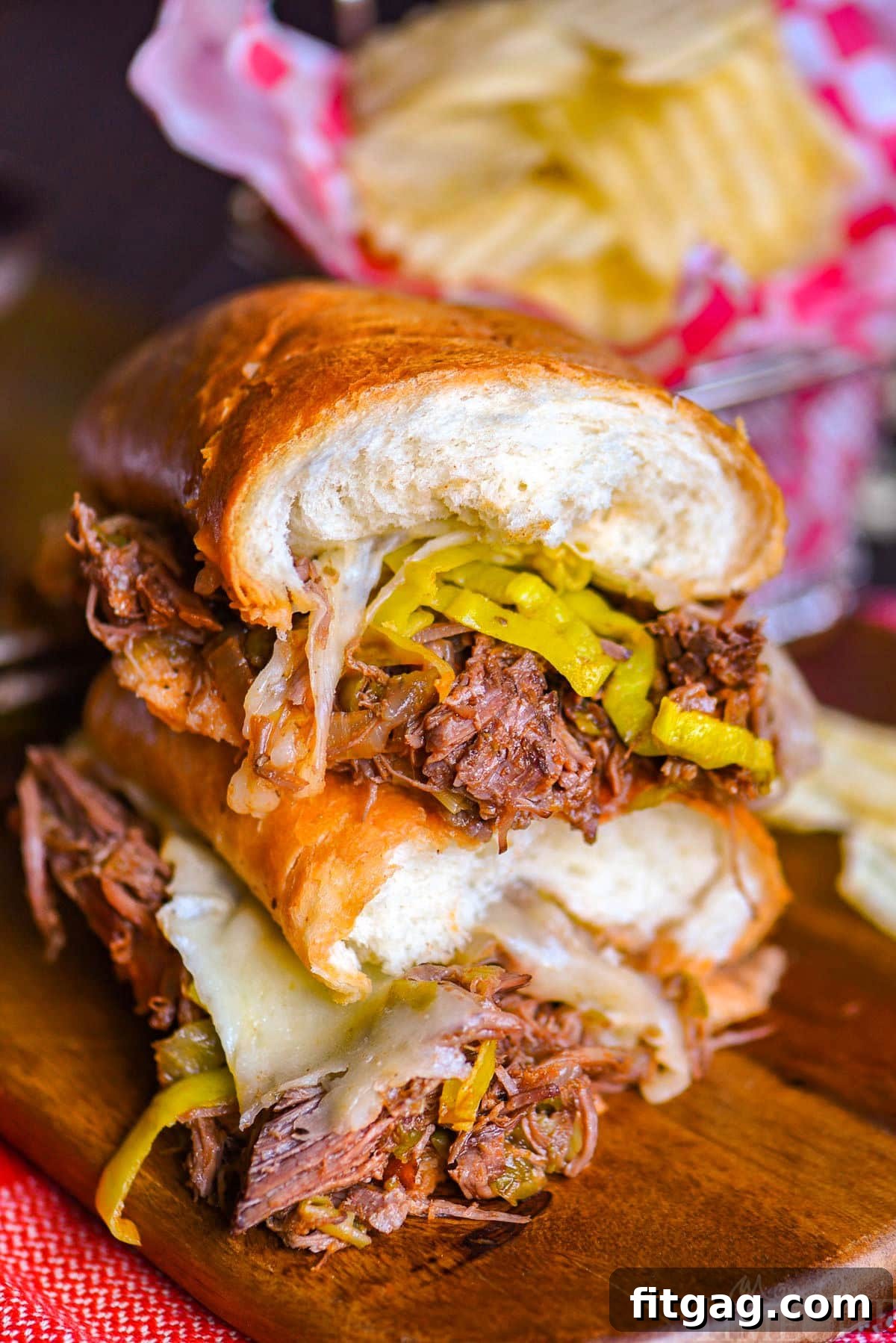 Melt-in-Your-Mouth Slow Cooker Italian Beef Sandwiches 3 Two halves of a Italian Beef sandwich stacked on top of each other with the melted Provolone cheese and pepperoncinis showing.