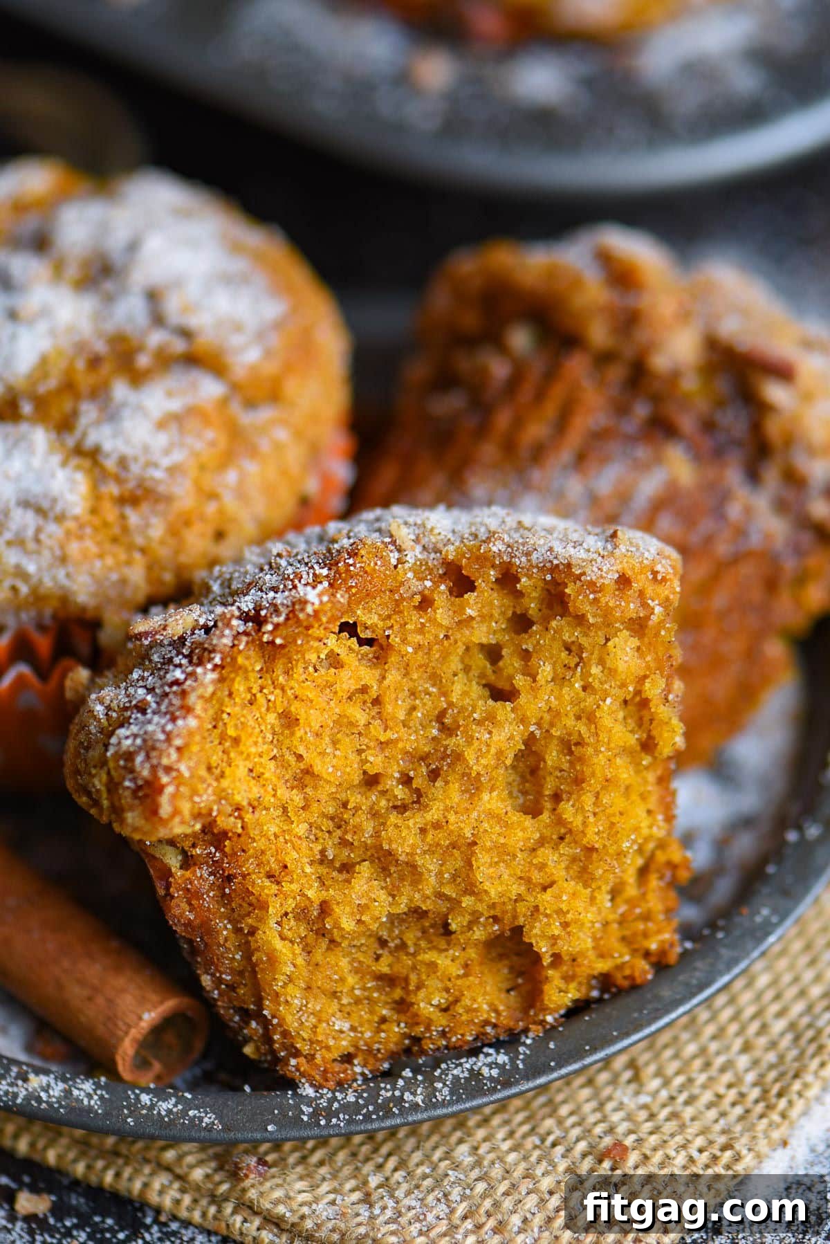 A close-up shot of a pumpkin muffin cut in half, elegantly placed on a metal plate, with more enticing muffins visible in the background, highlighting the soft interior and inviting texture.