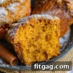 Close up shot of half a pumpkin muffin sitting on metal plate with more muffins behind it.