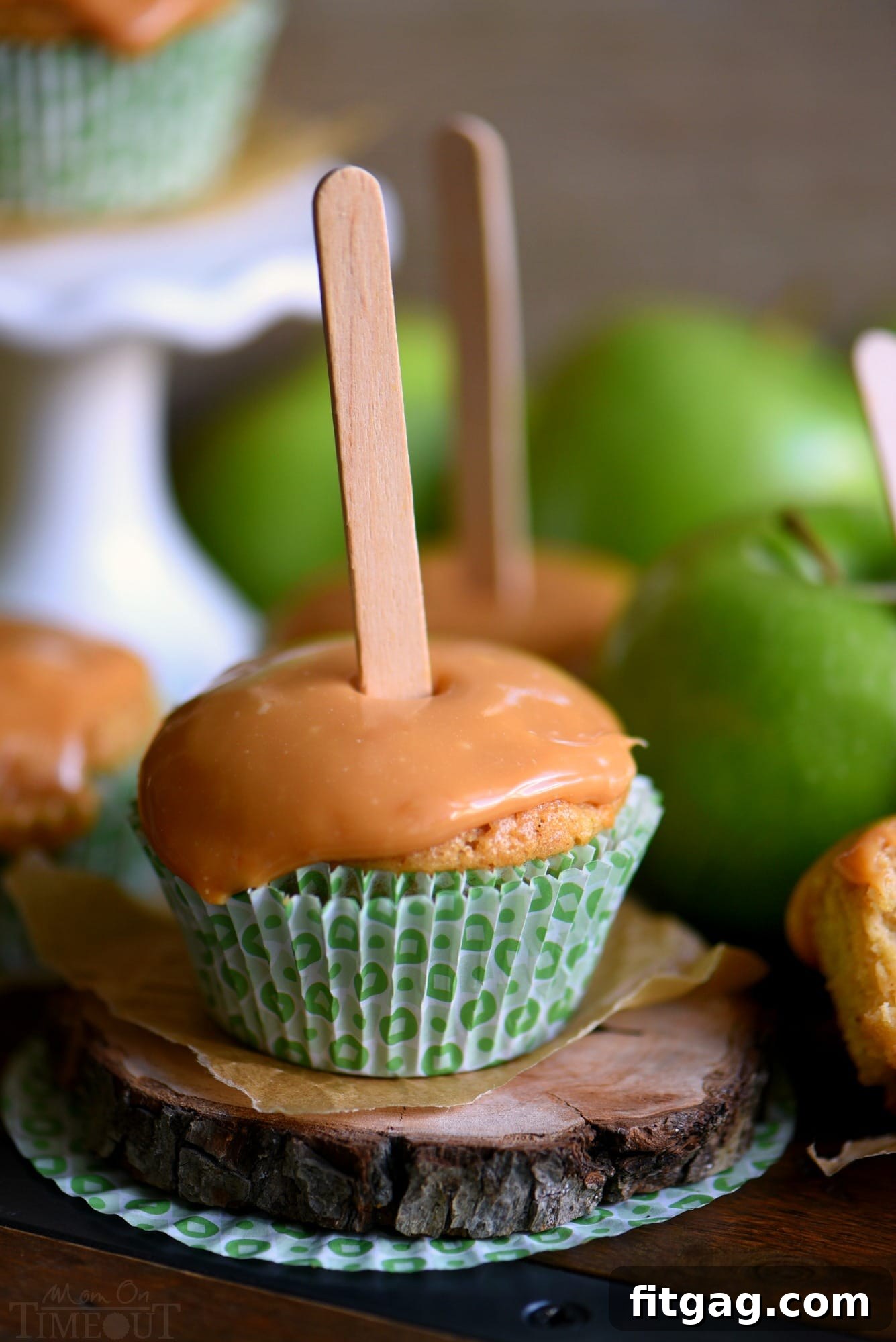 Autumn Caramel Apple Delights 4 A stunning display of caramel apple cupcakes, each adorned with creamy caramel frosting and a popsicle stick, symbolizing the perfect fall dessert. They are arranged on a rustic wooden surface, highlighting their rich colors and inviting texture. // Mom On Timeout