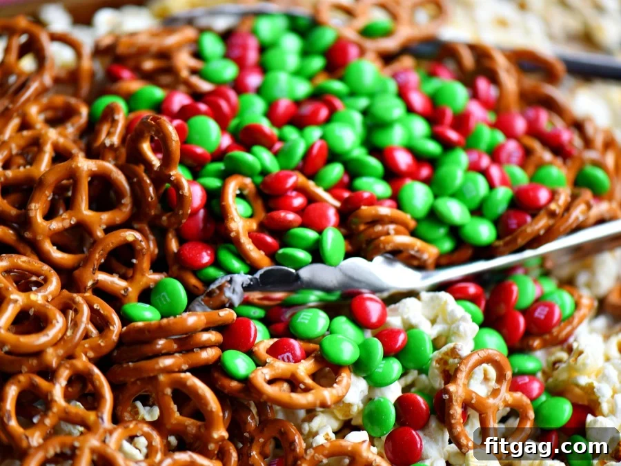 Close-up of a festive Snow Day Snack Mix featuring popcorn, pretzels, M&M's, marshmallows, and colorful sprinkles, coated in a sweet white candy shell. Ideal for holiday parties and gifting.