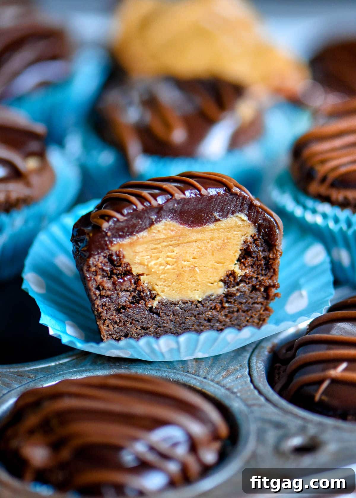 One Buckeye Bite, artfully cut in half, showcasing its layers of chocolate cookie, peanut butter filling, and ganache. It rests in a charming blue and white polka dot mini muffin liner.
