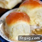 two fluffy dinner rolls sitting on a round white plate with gold trim.