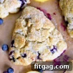 Top down view of a freshly baked lemon blueberry scone on parchment paper, surrounded by fresh blueberries