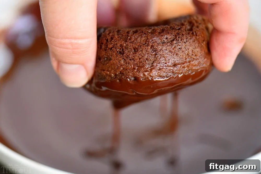 Close-up of a chocolate donut being dipped into a luscious, shiny chocolate glaze.