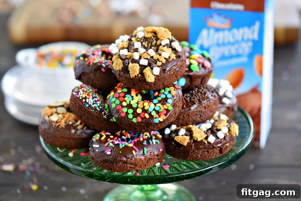 A stack of freshly baked chocolate cake mix donuts with a rich chocolate glaze and various toppings, served on a wire rack.