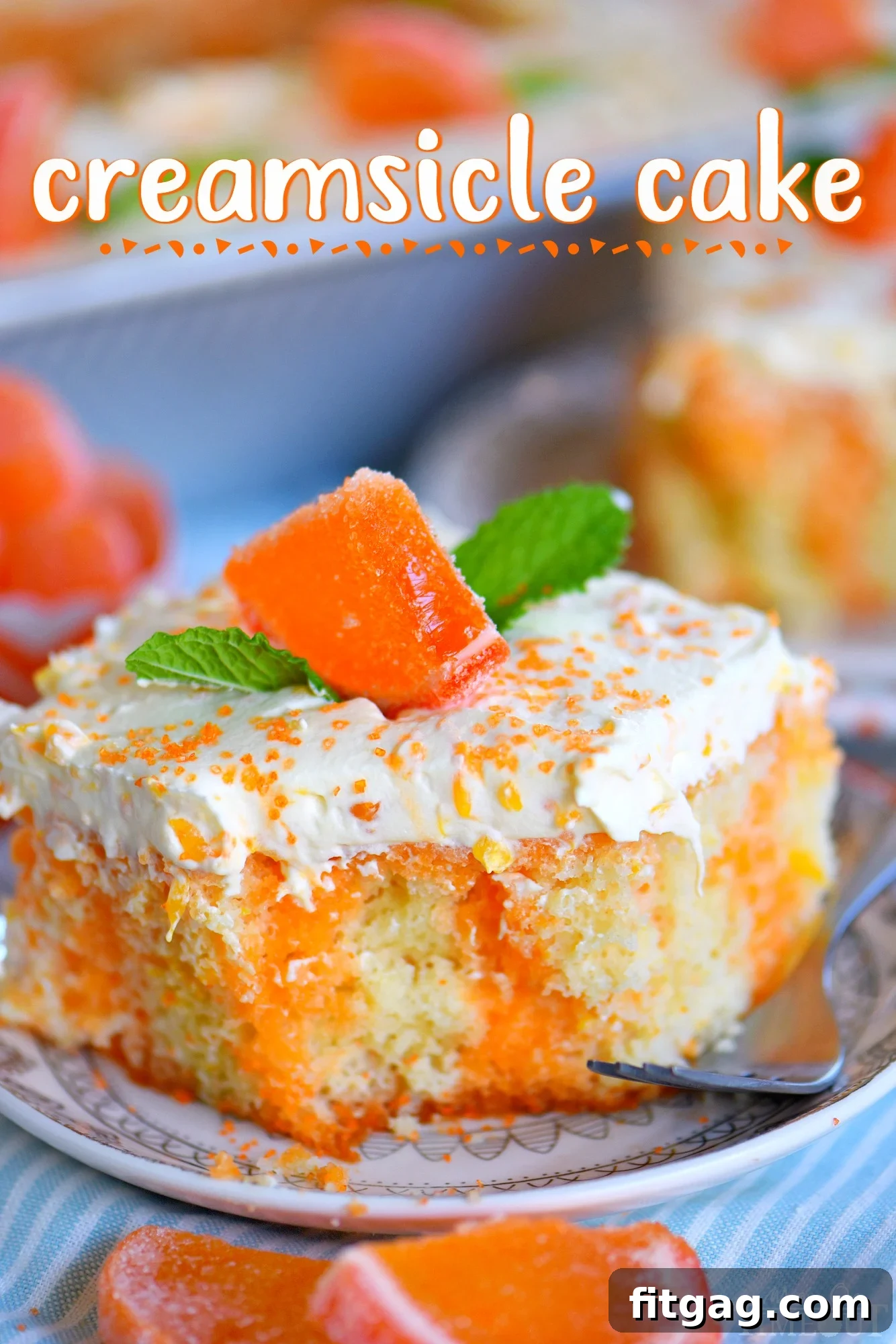 This easy Orange Creamsicle Poke Cake is a wonderful addition to all your summer parties! A lovely vanilla cake that is bursting with orange flavor and topped with a fluffy orange and vanilla frosting that no one will be able to resist! // Mom On Timeout #orange #creamsicle #cake #vanilla #dessert #desserts #cake #baking #summer A vibrant slice of Orange Creamsicle Poke Cake garnished with fresh mint leaves, served on a small white plate with a fork, highlighting its moist texture and dual-layer frosting.