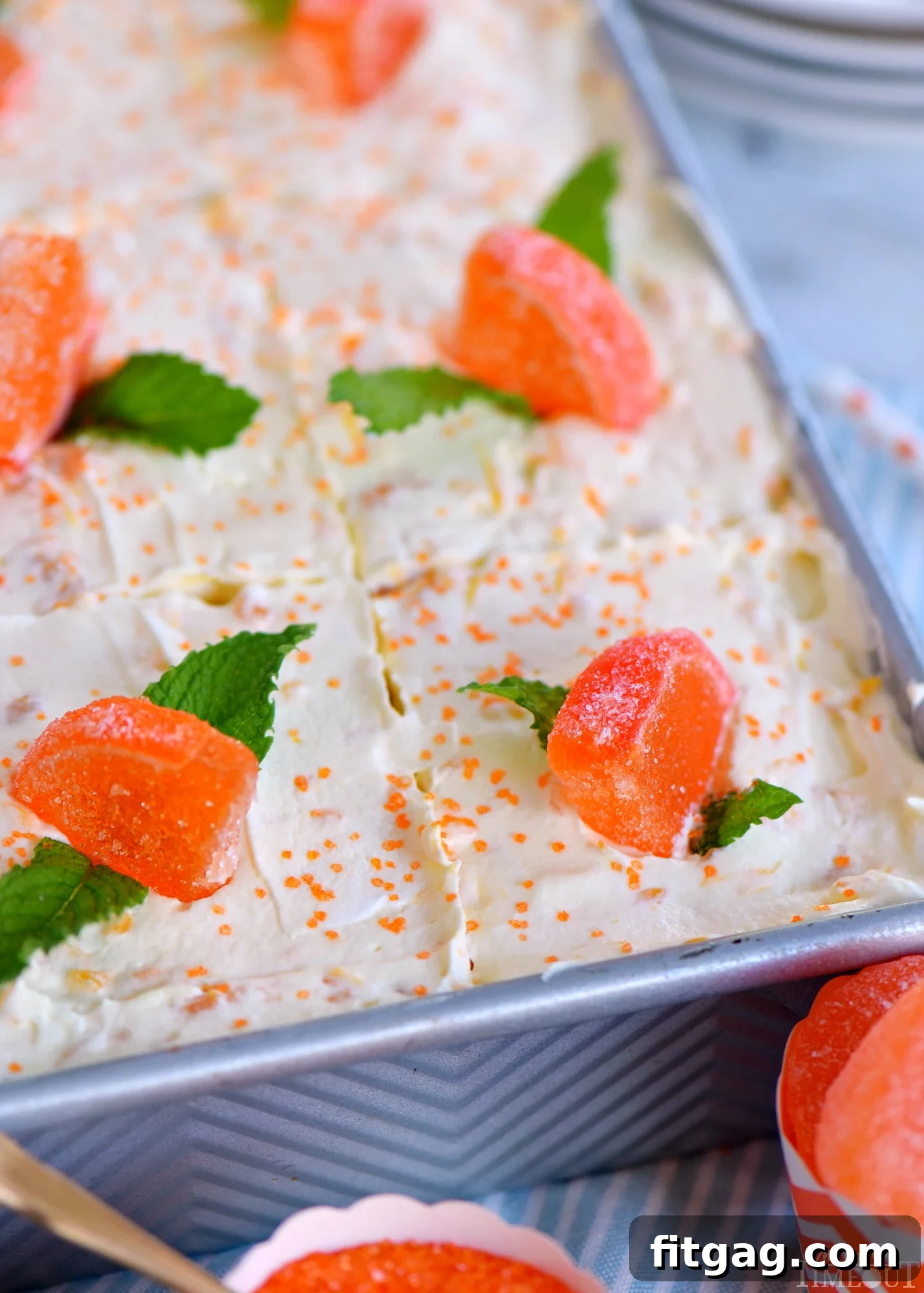 A beautiful whole Orange Creamsicle Poke Cake resting in a 9x13 metal baking dish, artfully garnished with sweet candy orange slices and fresh mint leaves, ready for serving.