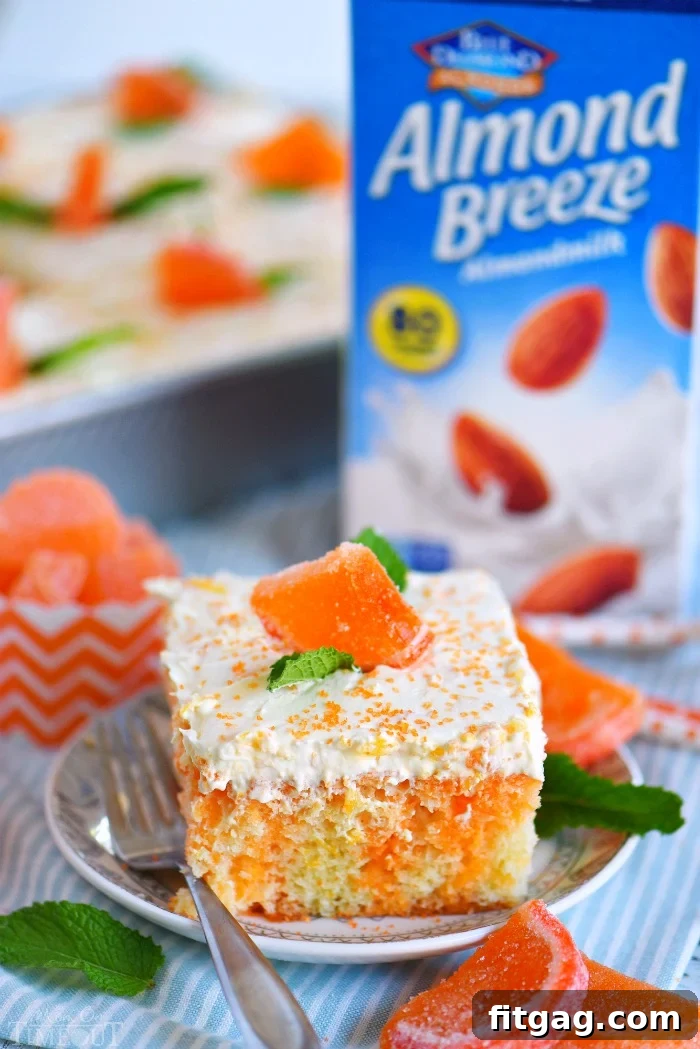 A delicious slice of Orange Creamsicle Poke Cake, beautifully garnished with fresh mint leaves and a candied orange slice, presented on a small plate next to a fork.