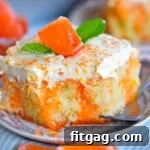slice of creamsicle cake on round white plate topped with fluff frosting and orange candy.
