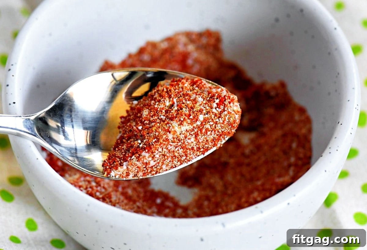 A small bowl holding a perfectly mixed seasoning blend, ready to be rubbed onto succulent chicken thighs. A spoon is poised above the bowl, showcasing the rich texture of the spice mixture.