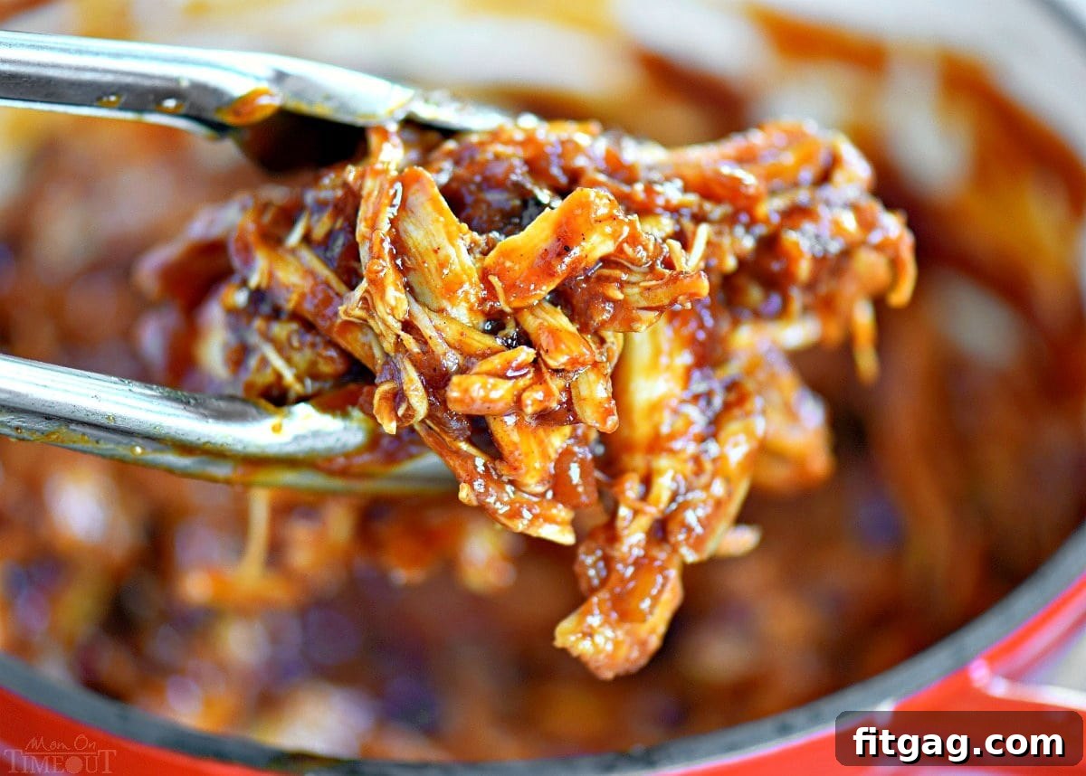 A generous serving of BBQ pulled chicken being held above a saucepan with tongs, showcasing its rich, saucy texture.