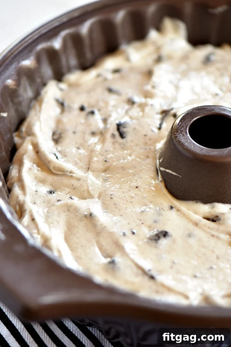 Rich Oreo cake batter, generously speckled with crushed cookies, poured into a decorative bundt pan, ready for baking.