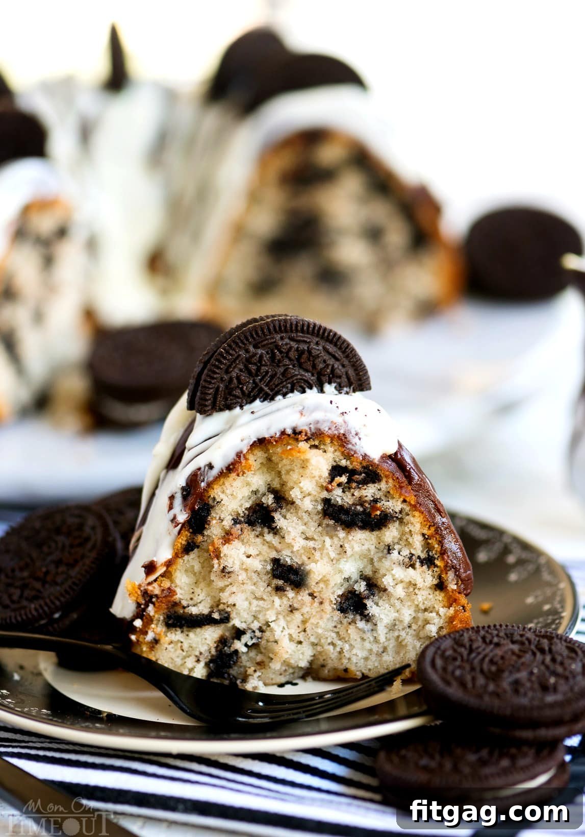 A close-up of a generously glazed slice of Cookies and Cream OREO Bundt Cake, topped with a whole Oreo, ready to serve.