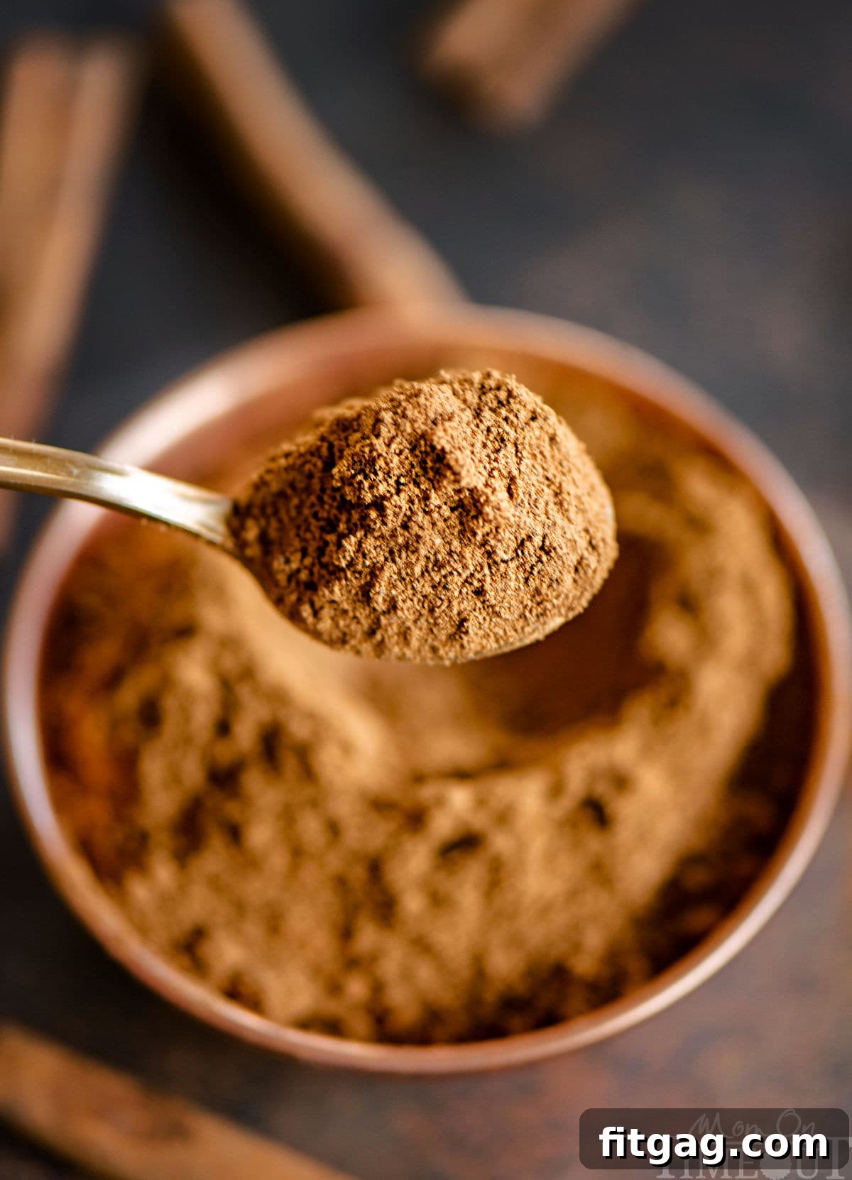 Spoonful of pumpkin pie spice held up over bowl where five spices were mixed together.