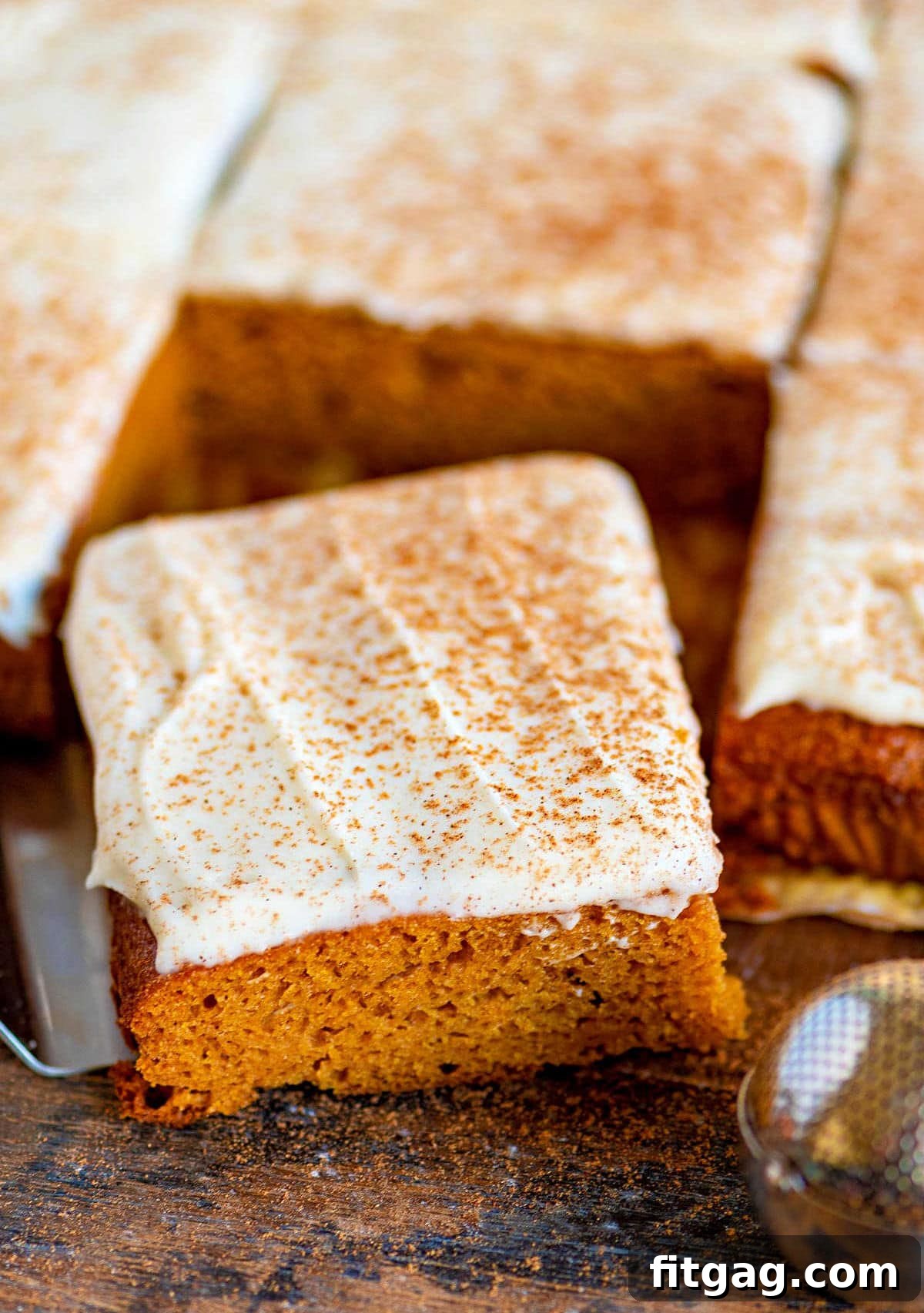 Dreamy Spiced Pumpkin Bars 2 Perfectly cut pumpkin bars, each square topped with a generous swirl of brown butter cream cheese frosting and a sprinkle of pumpkin pie spice, resting on a dark wooden board.