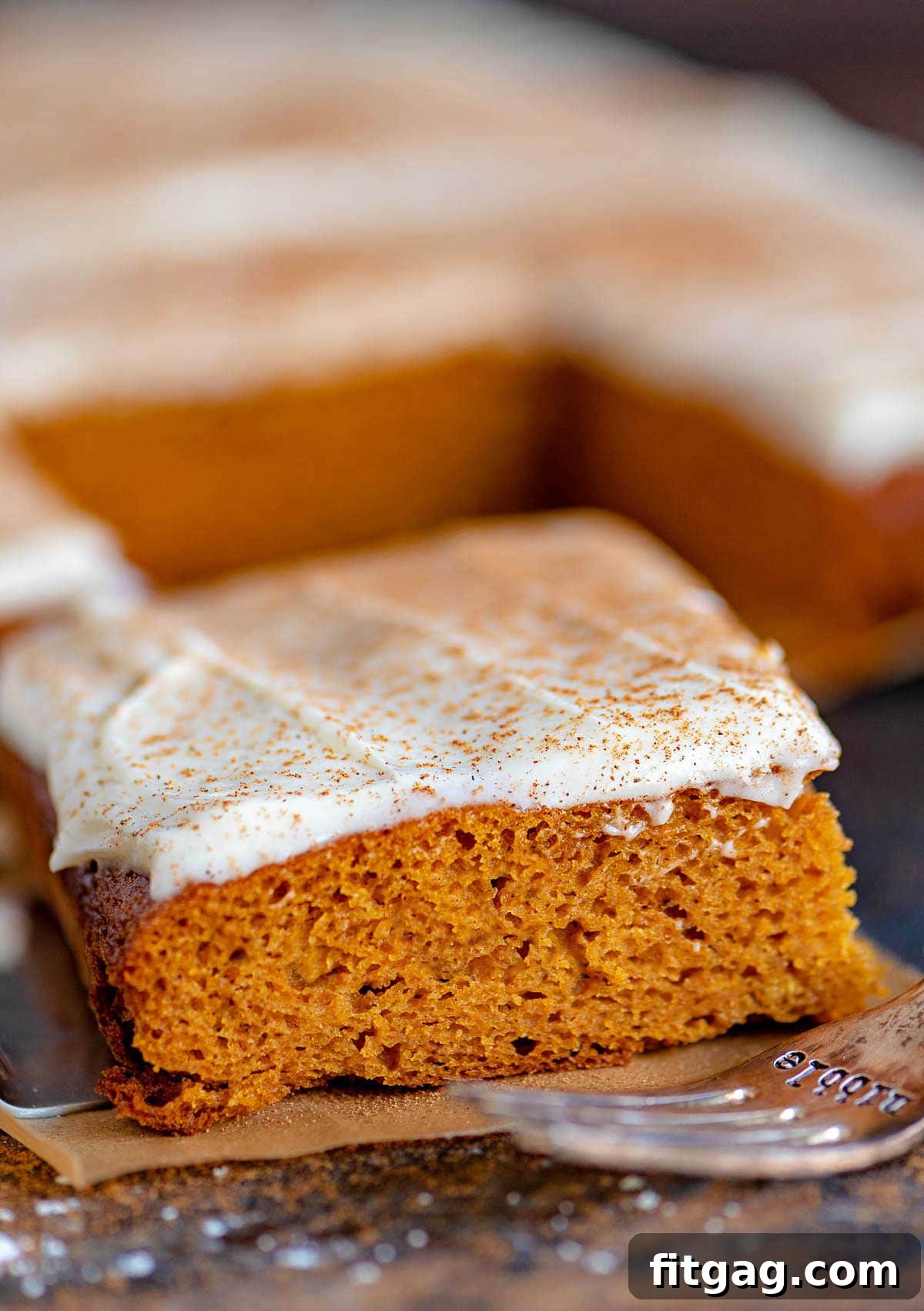 Dreamy Spiced Pumpkin Bars 6 A single square of pumpkin bar with brown butter cream cheese frosting and spice, resting on parchment paper with an antique fork.