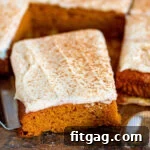 Dreamy Spiced Pumpkin Bars 7 pumpkin bars cut into squares sitting on dark wood board with pumpkin pie spice dusted over the cream cheese frosting.
