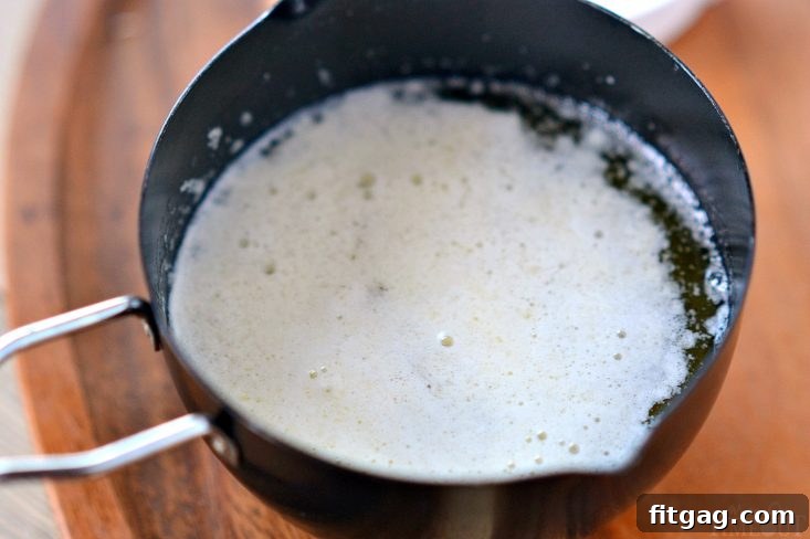 White foamy milk solids rising to the surface of melted butter in a saucepan.