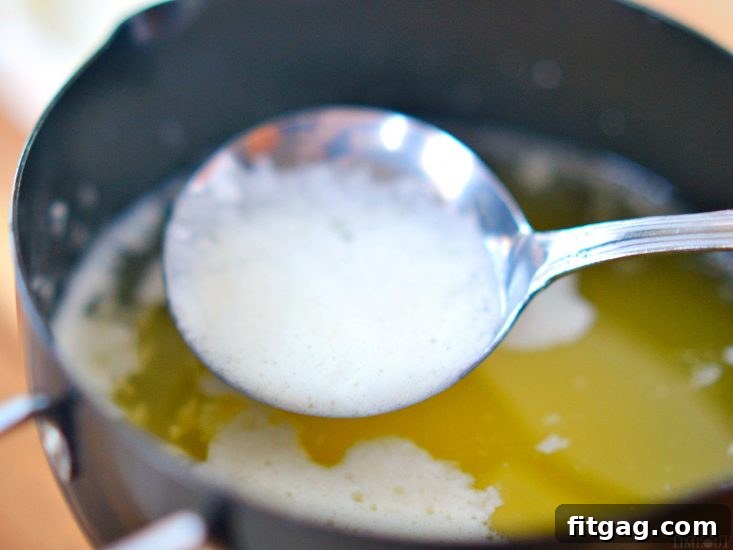 A spoon gently skimming the foamy milk solids from the surface of simmering butter.