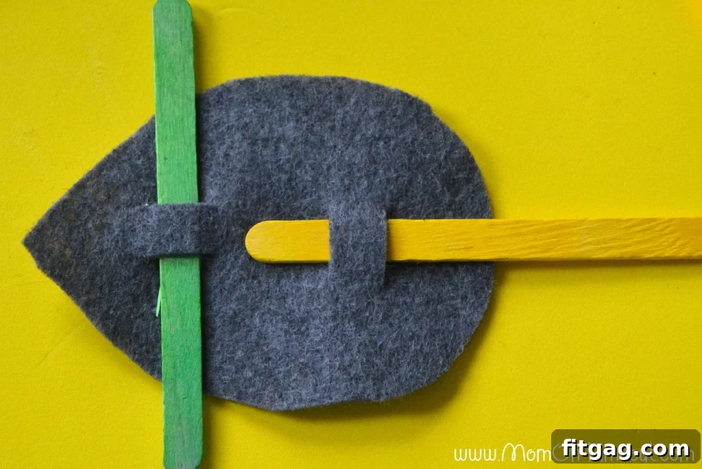 A felt mouse body with green and yellow popsicle sticks indicating the placement of ears and candy cane tail.