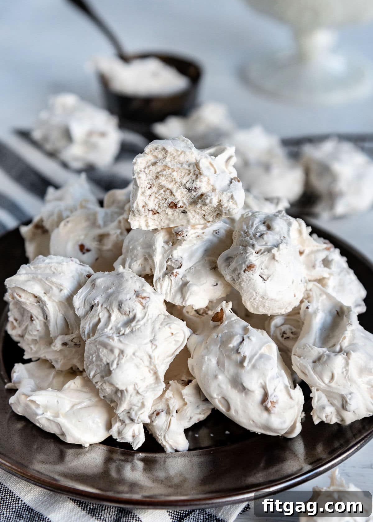 A silver plate piled high with delicate, white divinity candy, with one piece broken in half to reveal its soft texture.