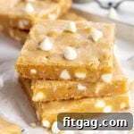 three blondie bars stacked with white chocolate chips sprinkled about sitting on white parchment with more bars in the background.