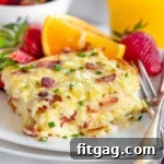 Serving of hash brown breakfast casserole on white round plate with fresh orange wedge and strawberries behind it.