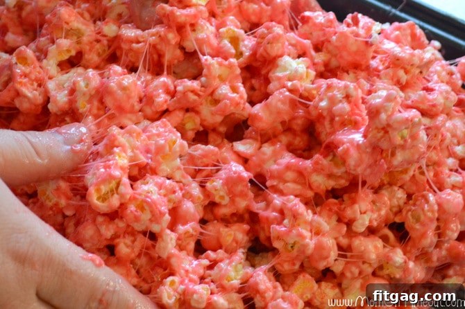 Hands mixing sticky marshmallow popcorn mixture