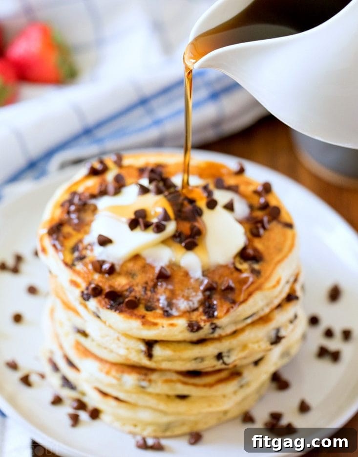 syrup being poured onto a stack of chocolate chip pancakes