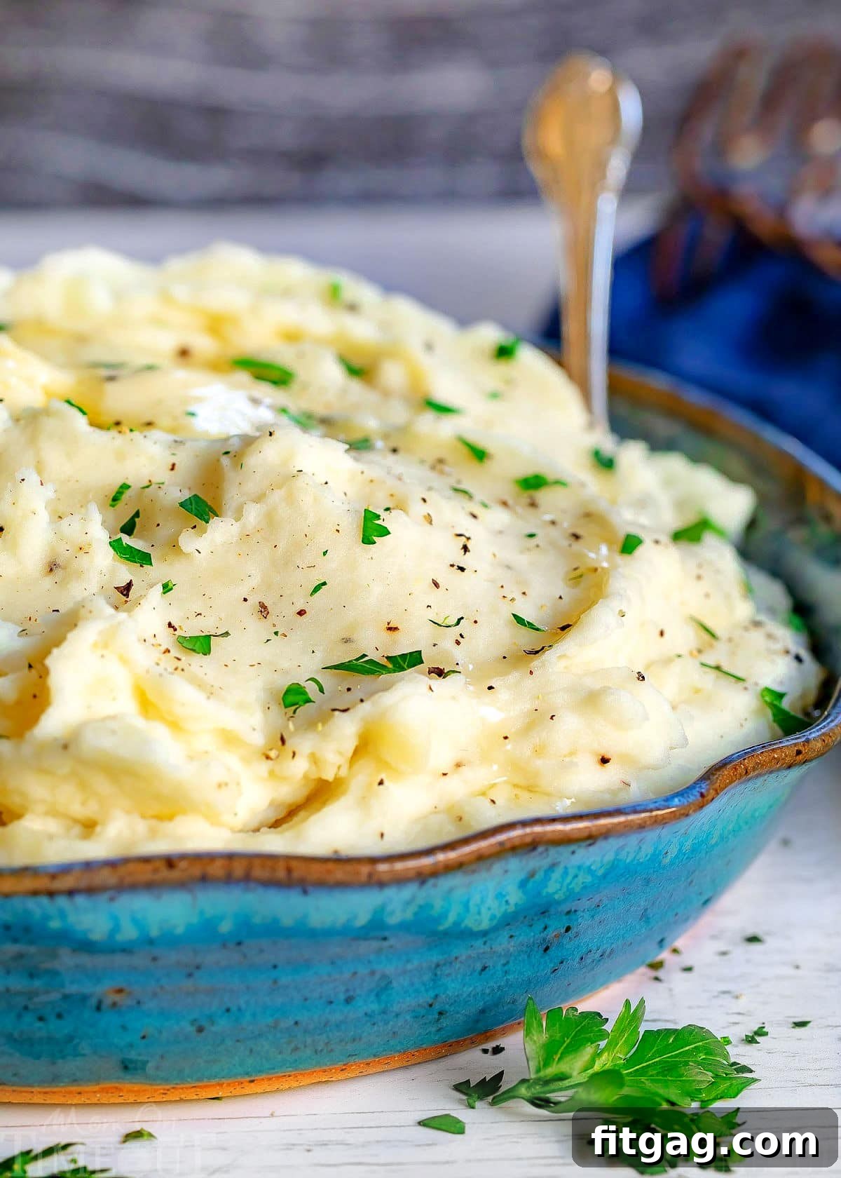 front view of large blue bowl of creamy mashed potato recipe topped with fresh parsley and butter.