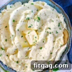 top down look at a blue and green bowl filled with fluffy mashed potatoes. slices of butter, pepper and chopped parsley garnish the mashed potatoes.