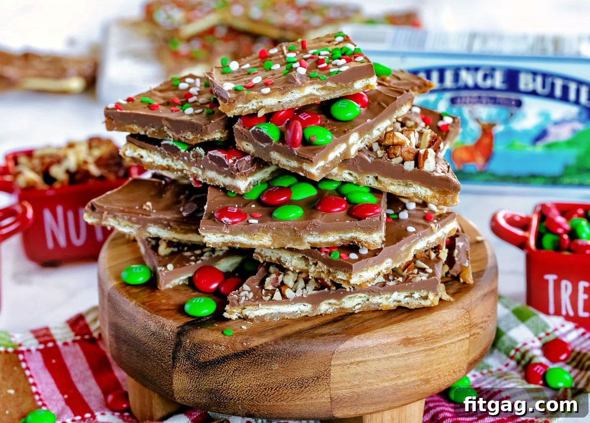 Christmas Toffee Craze 6 Delightful pieces of Christmas Crack saltine cracker toffee, adorned with colorful sprinkles and mini M&M's, are artfully arranged on a round wooden board. The board rests on a festive Christmas-themed napkin, creating a charming holiday tableau.