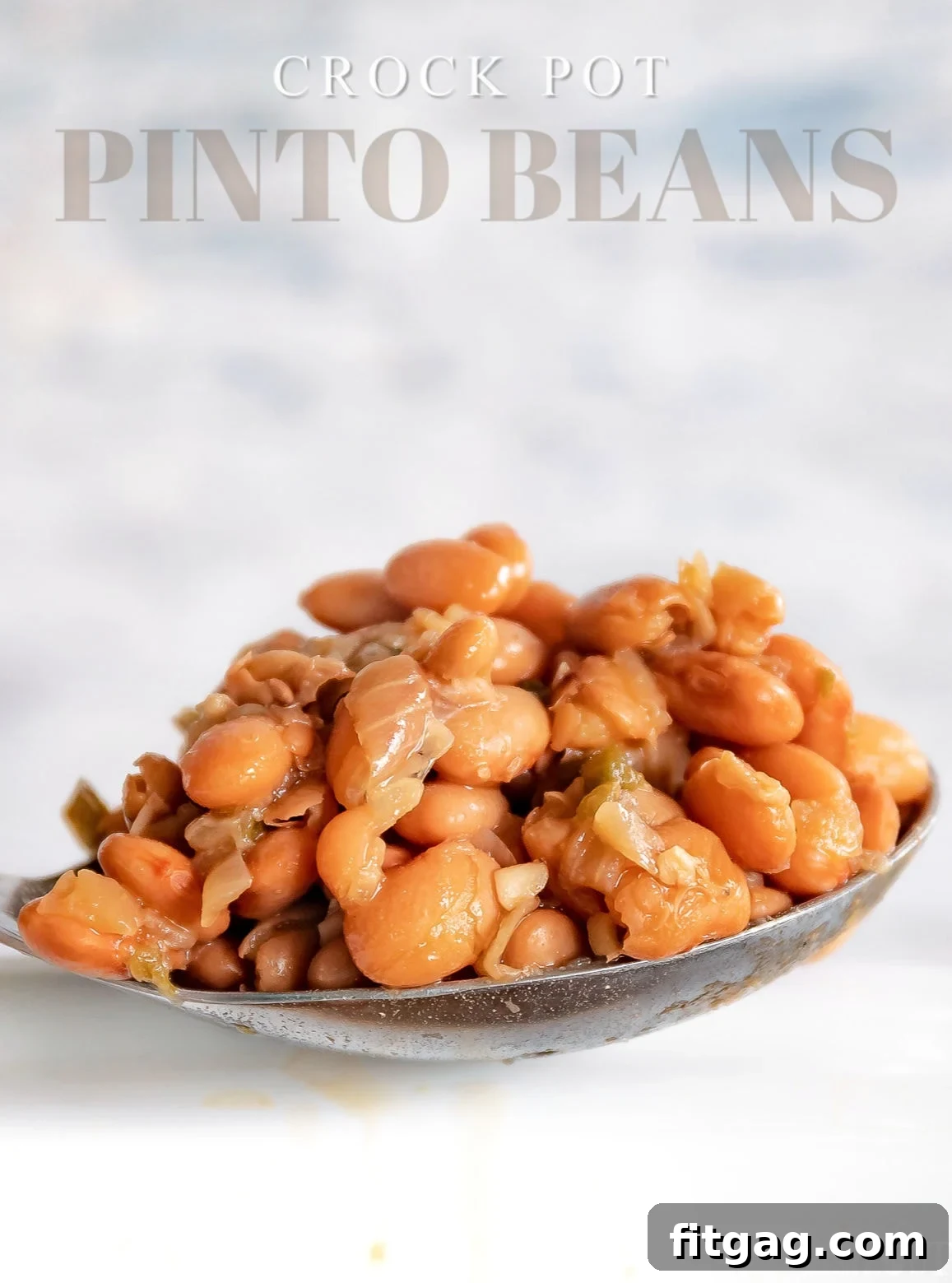 A serving spoon lifting perfectly cooked pinto beans from a white crockpot, with a text overlay indicating the recipe.