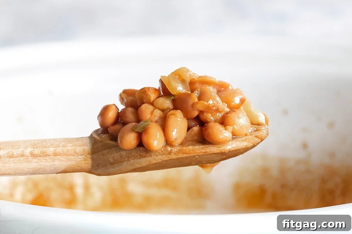 Close-up of crock pot pinto beans being scooped onto a wooden spoon, held over a white slow cooker.