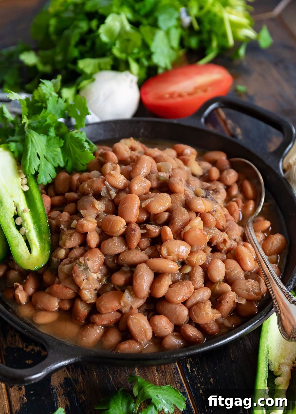 A black bowl of slow cooker pinto beans garnished with fresh jalapeño, diced tomato, and cilantro, served with a spoon.