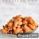 A serving spoon lifting perfectly cooked pinto beans from a white crockpot, indicating the recipe details.