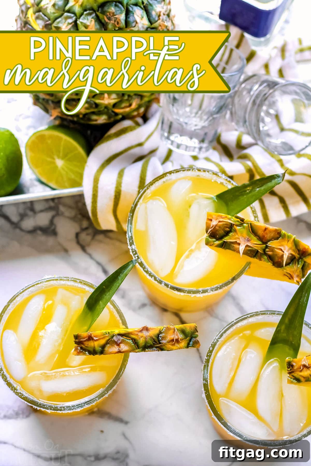 Pineapple Paradise Margarita 2 Two pineapple margaritas on a marble cutting board with a whole pineapple in the background, garnished with fresh pineapple wedges and lime slices.