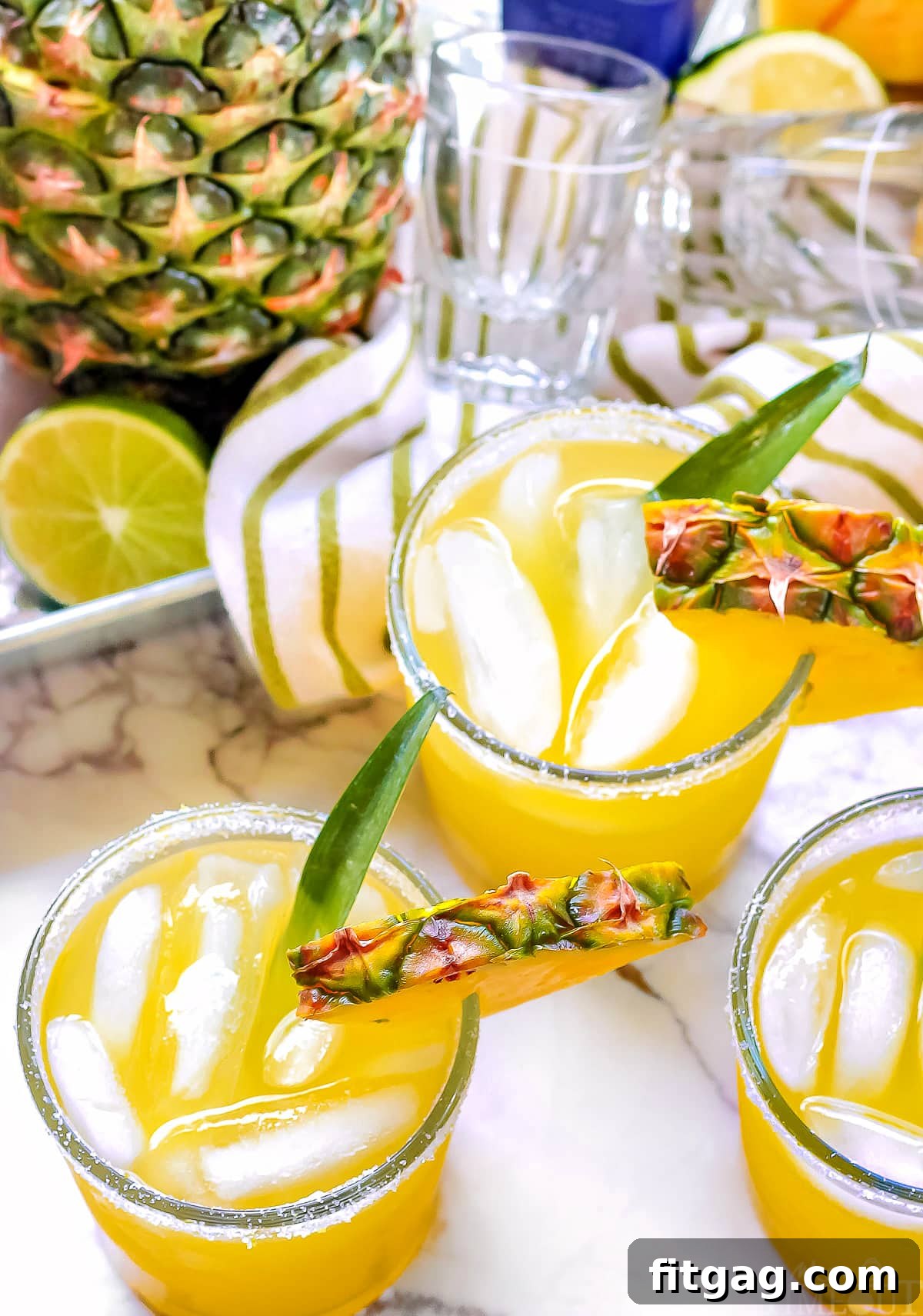 three pineapple margaritas on white marble garnished with pineapple wedges