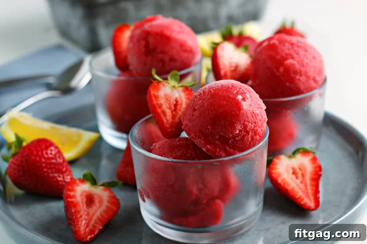 Ruby Frost 6 Easy strawberry sorbet recipe displayed in three small glasses on a gray plate, garnished with halved fresh strawberries, perfect for a refreshing treat.
