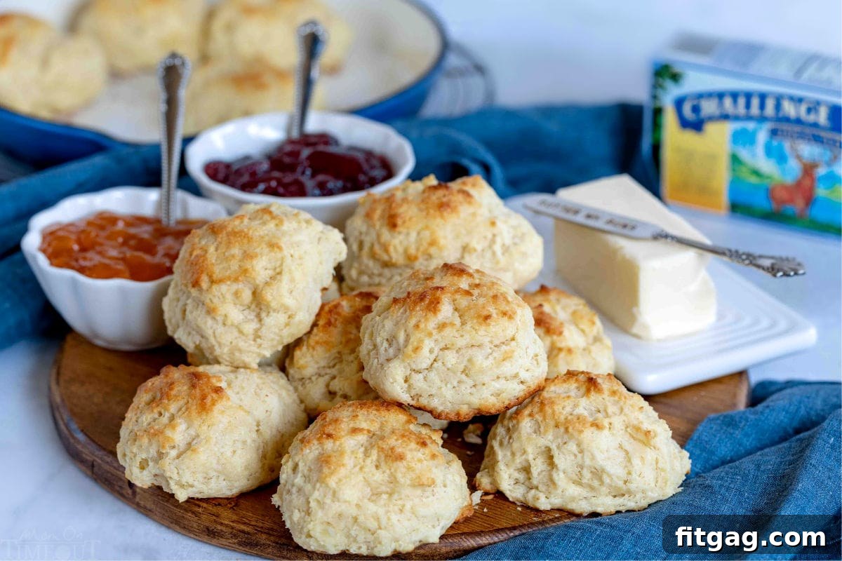 Freshly baked drop biscuits arranged on a wooden board, accompanied by jars of sweet jelly and a pat of butter, inviting a delicious meal.