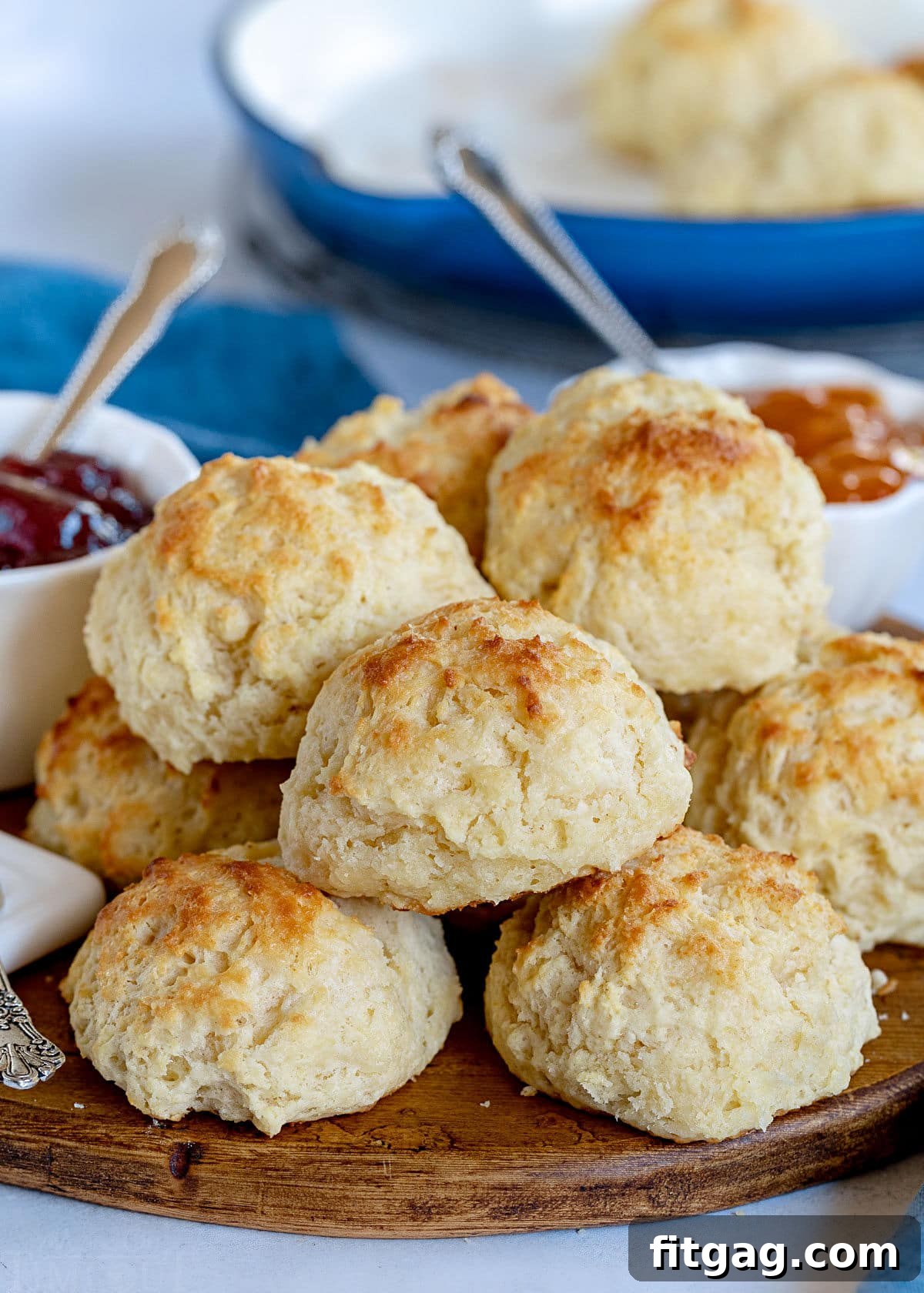A large pile of golden brown, fluffy drop biscuits displayed on a round wooden cutting board, inviting guests to enjoy.