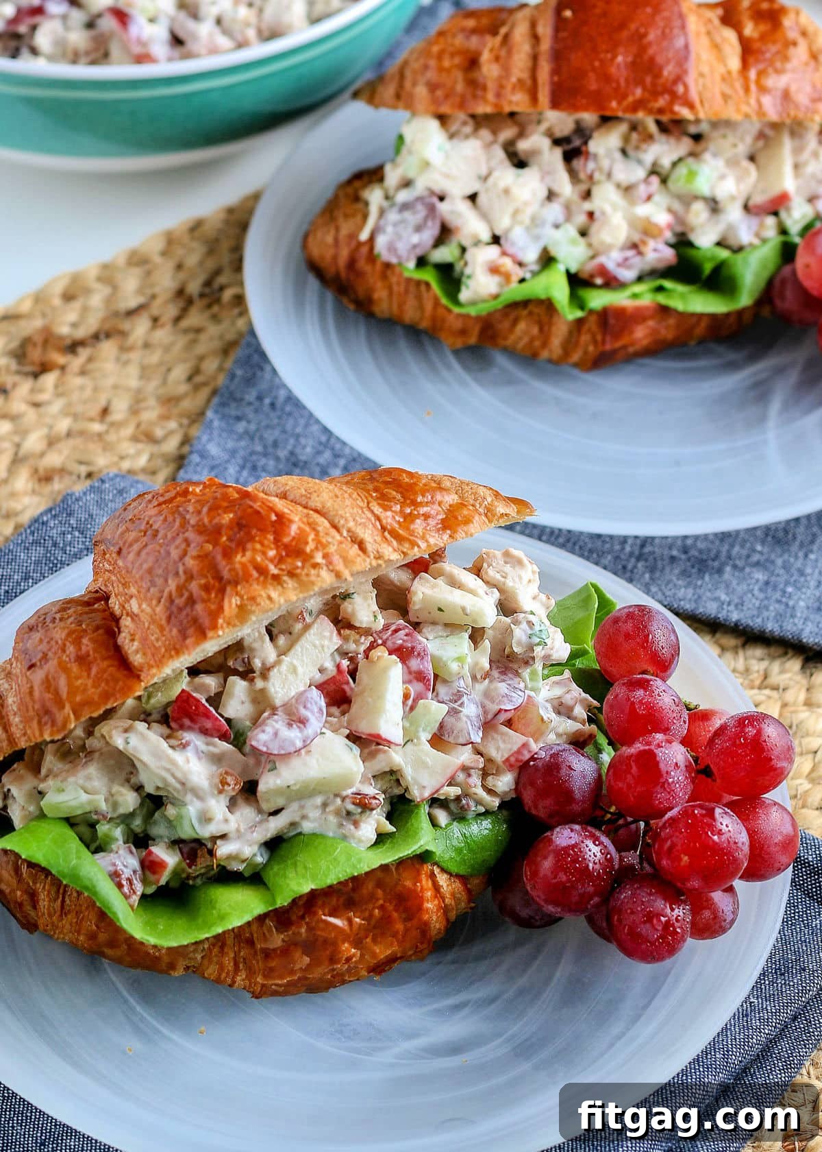 Two perfectly assembled chicken salad sandwiches served on white plates with elegant blue napkins, ready to be enjoyed.