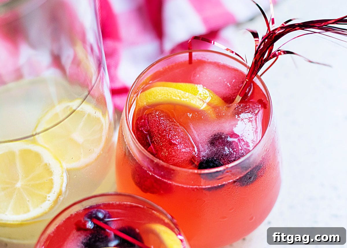 Two glasses of berry lemonade served alongside a pitcher of the same drink, ready for serving.