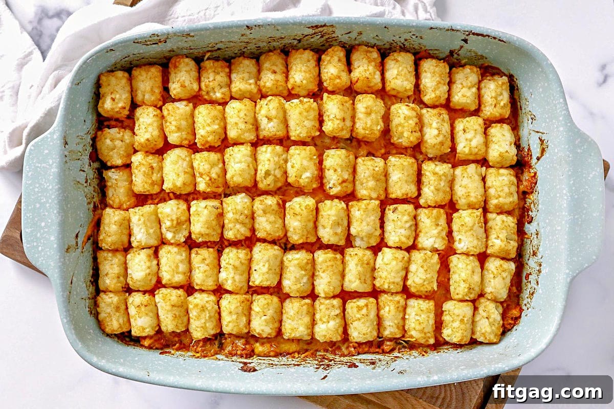 Fiesta Tater Tot Bake 3 A baked Taco Tater Tot Casserole in a casserole dish, resting on a rustic wooden cutting board, ready to be served.